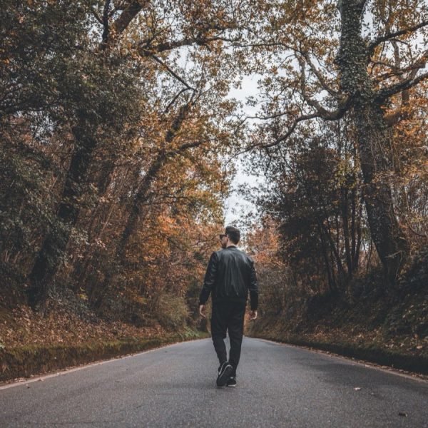 A person walking down a road through autumn woodland, seen from behind