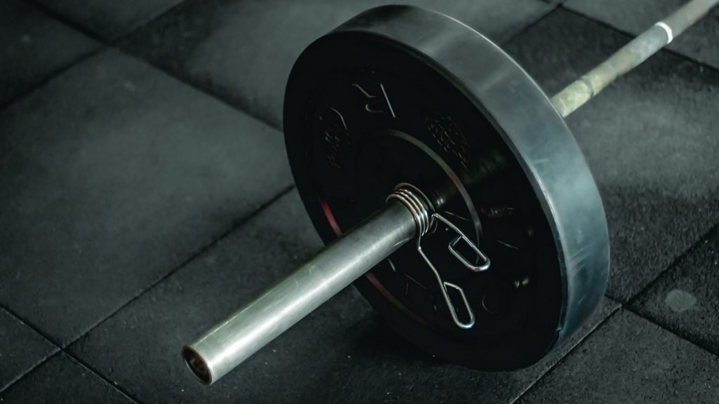 A barbell with a weight plate resting on a dark gym floor