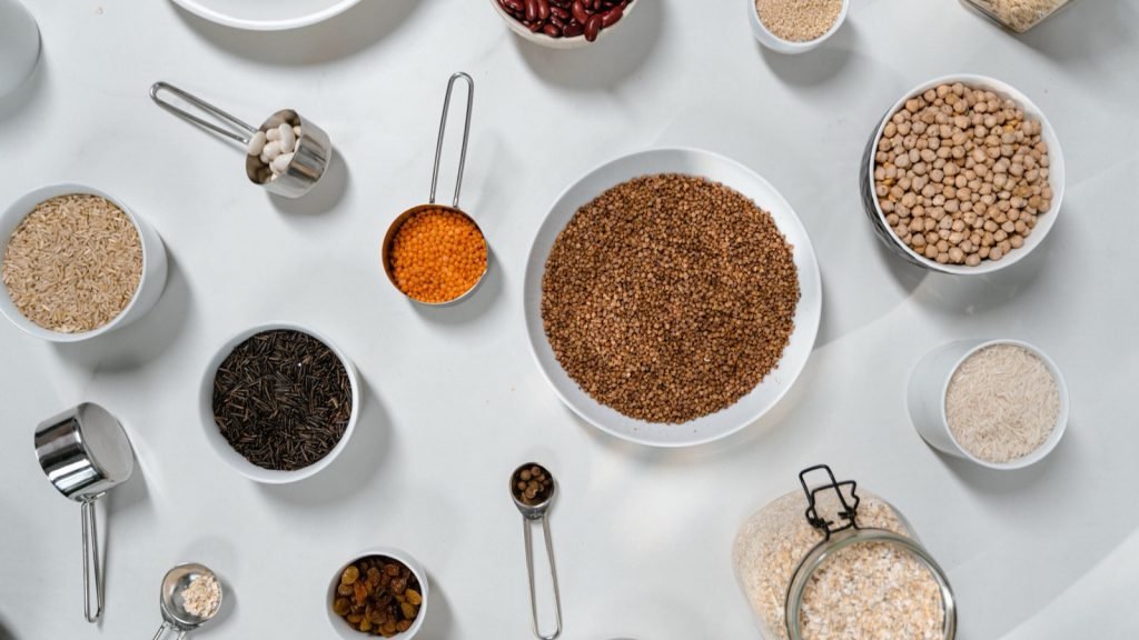 Bowls of grains, lentils and beans seen from above on a white table