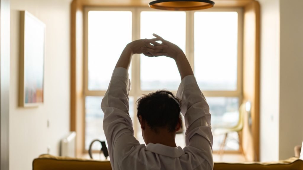 A person stretching their arms overhead in front of a sunlit window