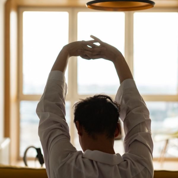 A person stretching their arms overhead in front of a sunlit window
