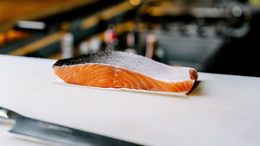 A fresh salmon fillet resting on a board in a kitchen